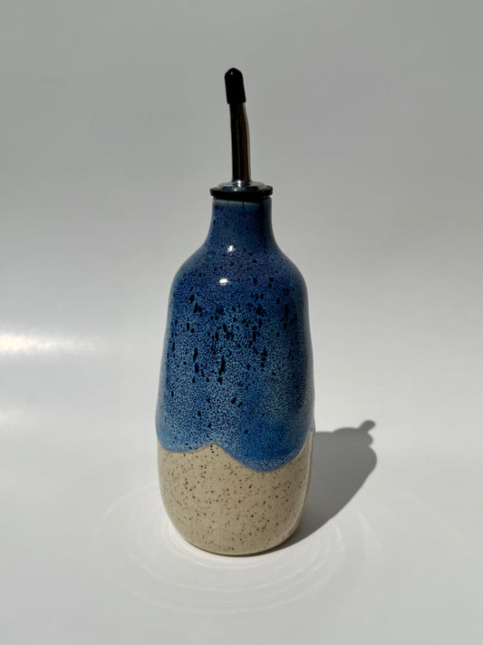 Blue speckled ceramic bottle with a beige base on a white background