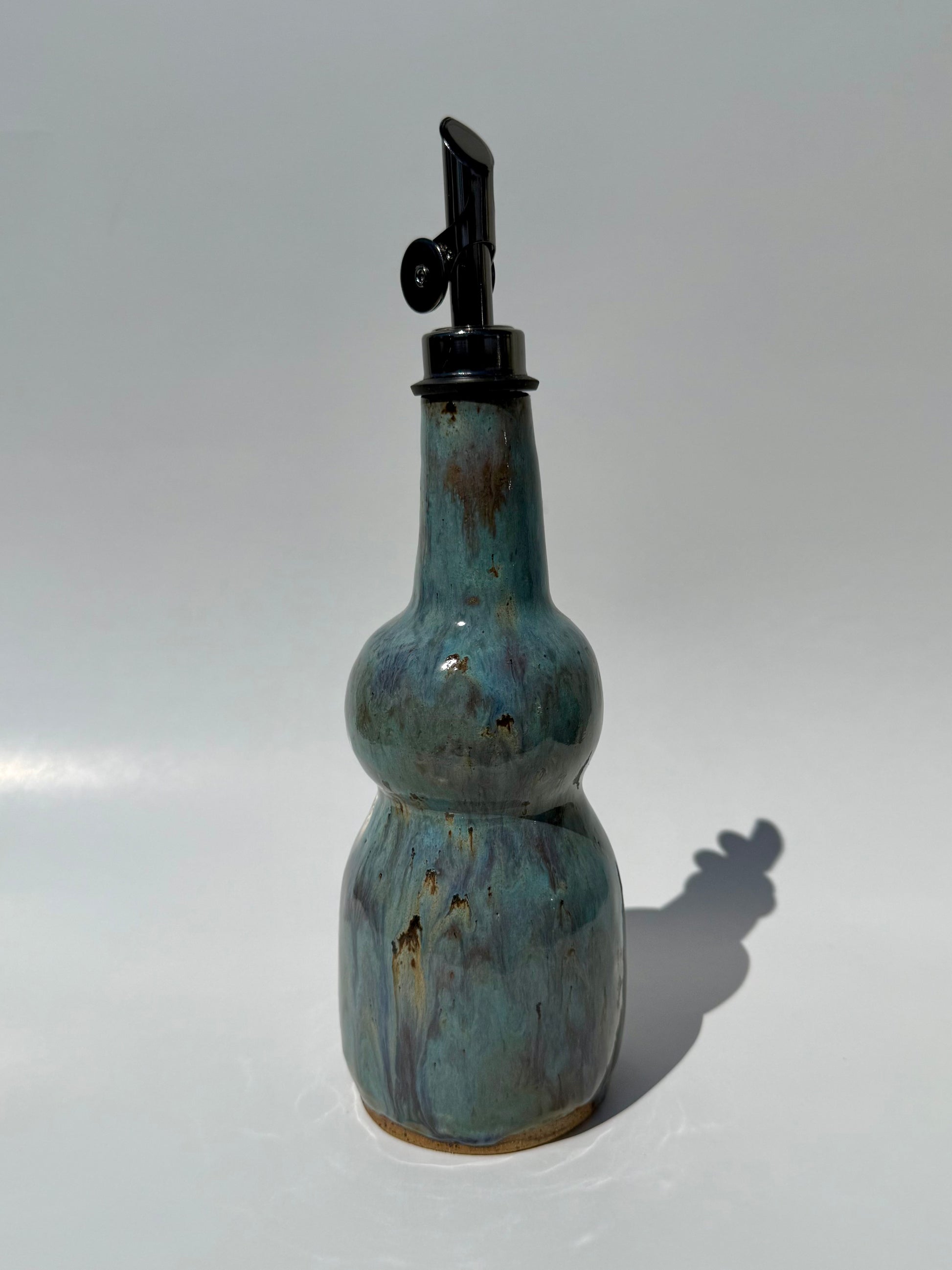 Blue ceramic oil bottle with a black cap on a white background