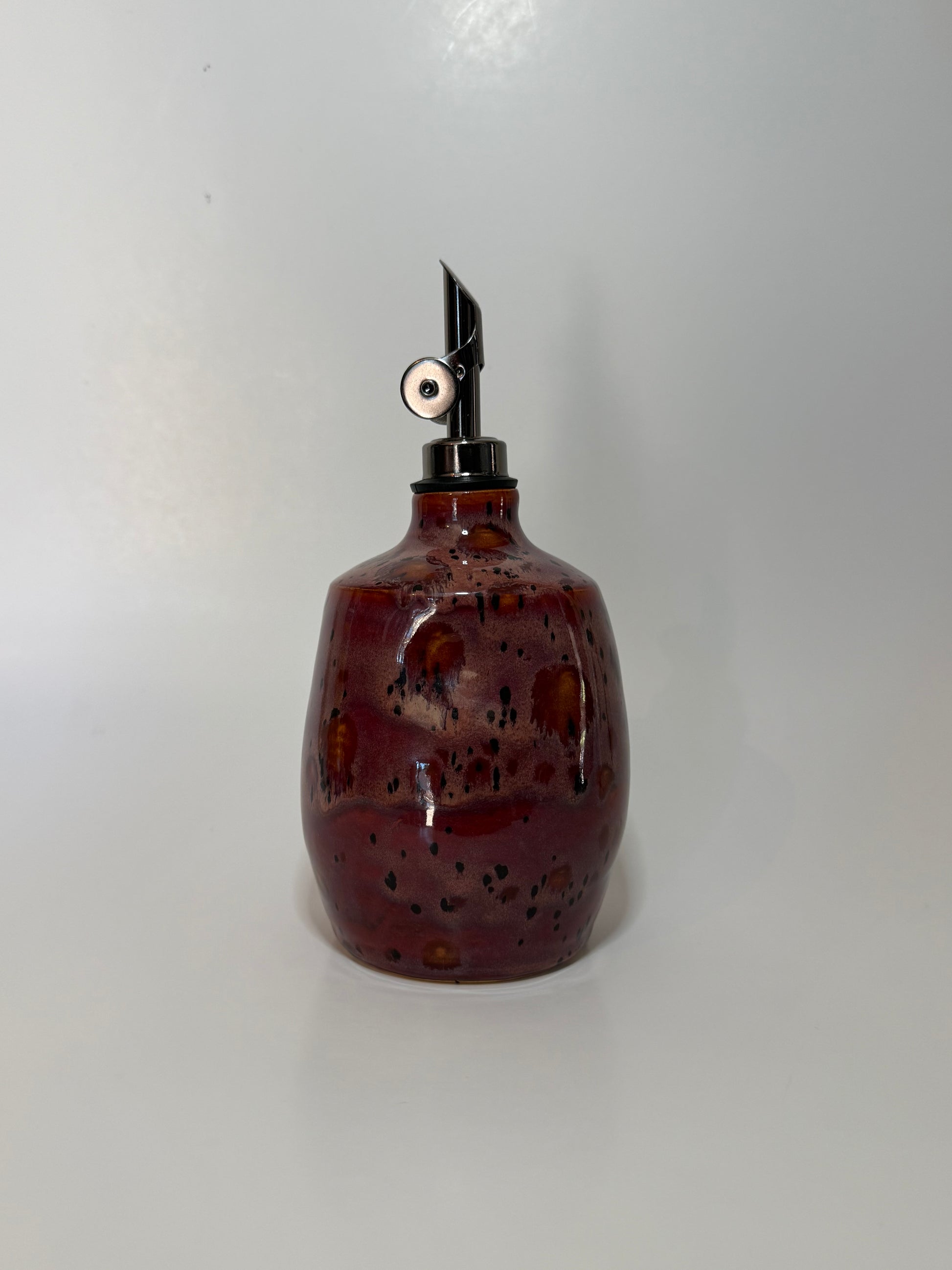 Red with Brown speckled ceramic oil bottle with a metallic nozzle on a white background